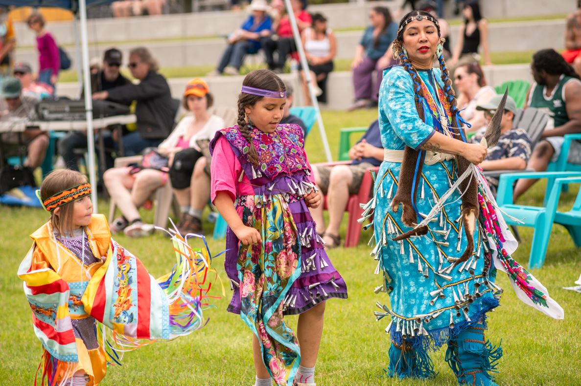 Two children (left) and one adult performing in full regalia.