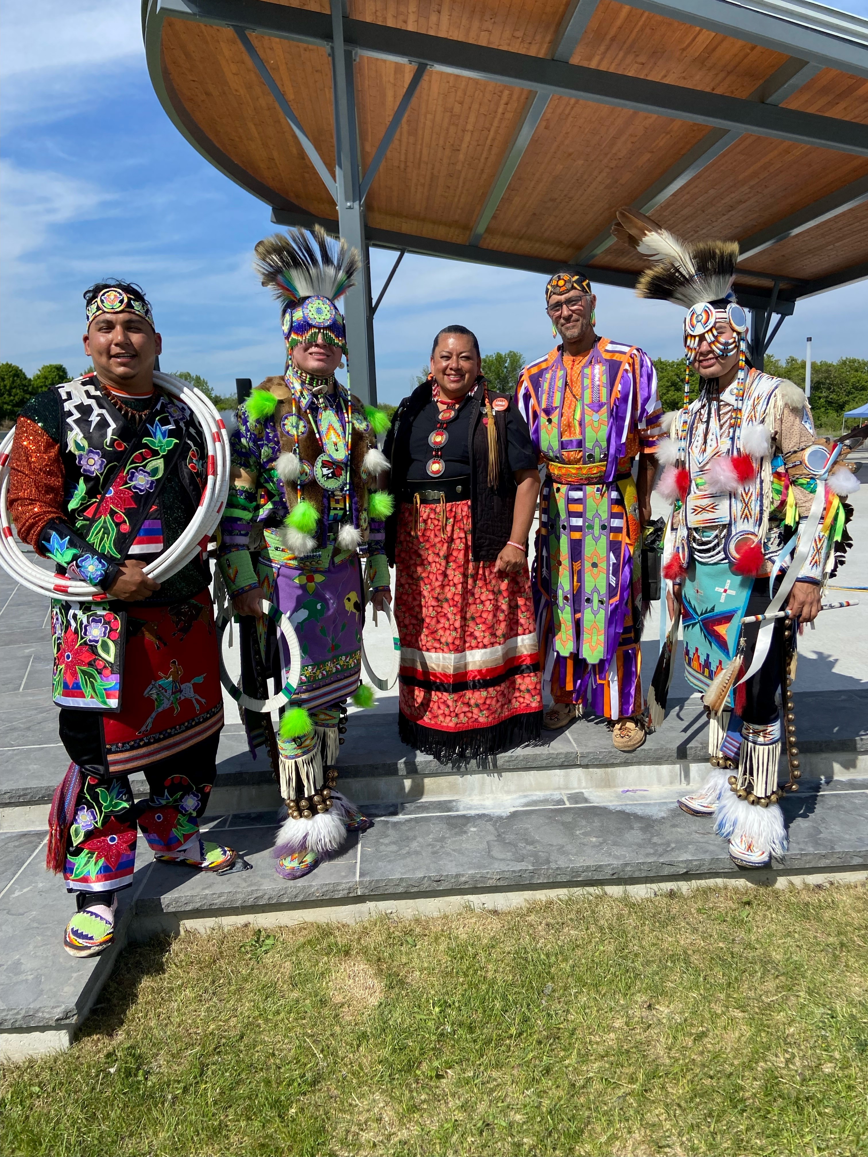 Five indigenous people smiling in traditional regalia.